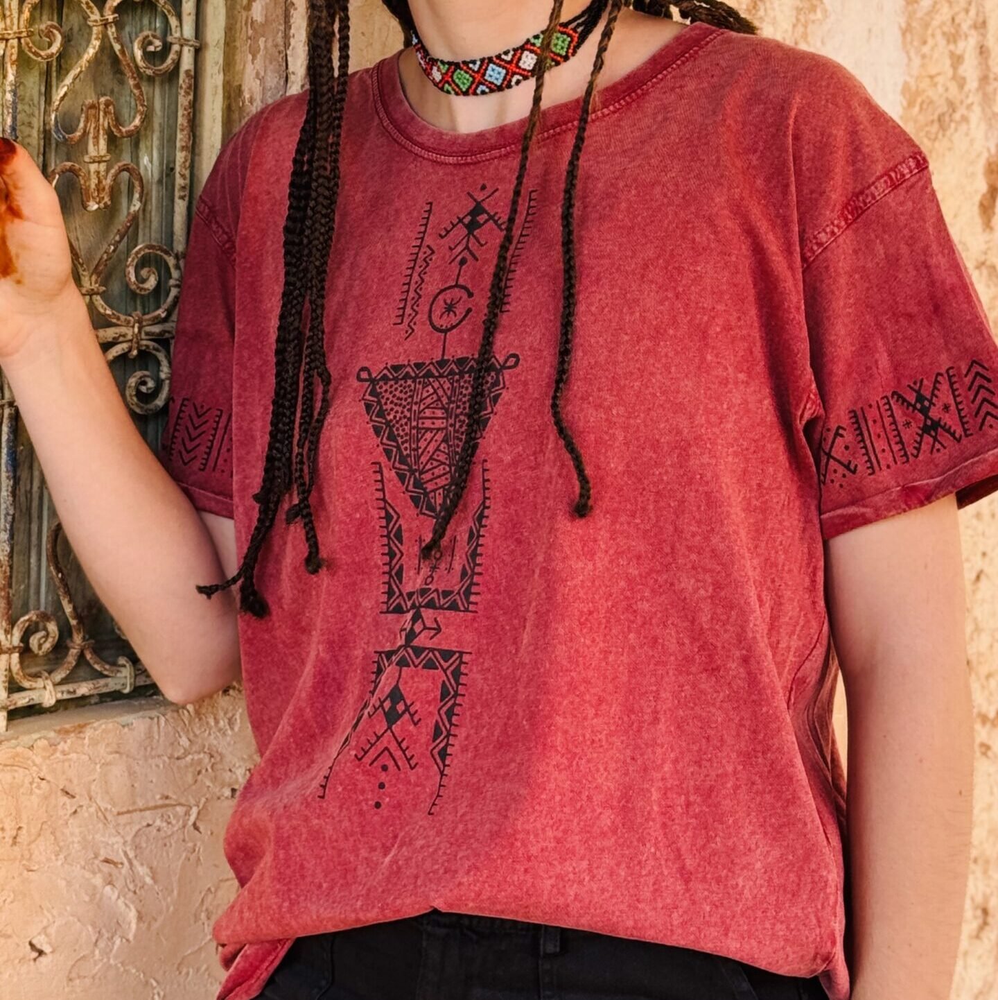 Pink Amazigh T-shirt with black Tifinagh-inspired geometric embroidery and central cultural symbol.