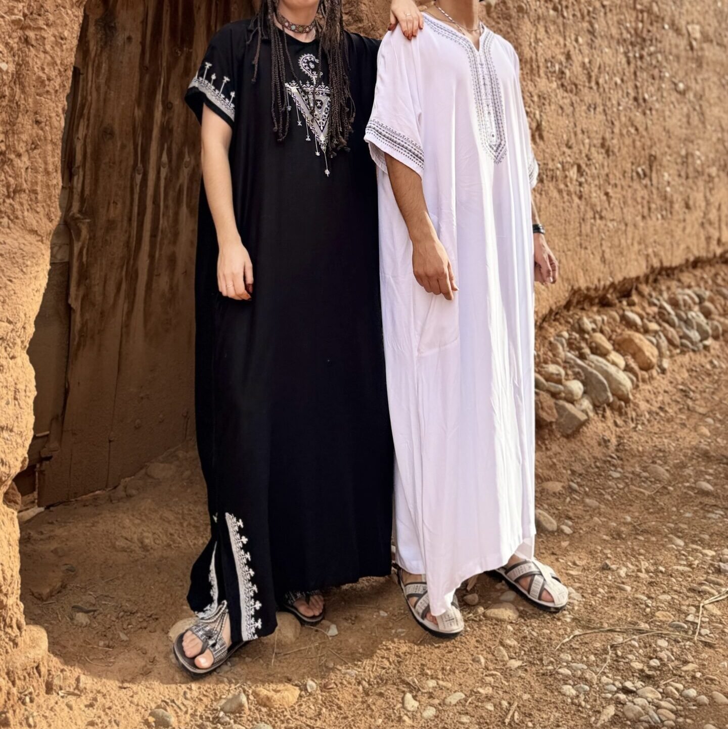 Black and white Moroccan Amazigh robes with geometric embroidery at a traditional earthen doorway