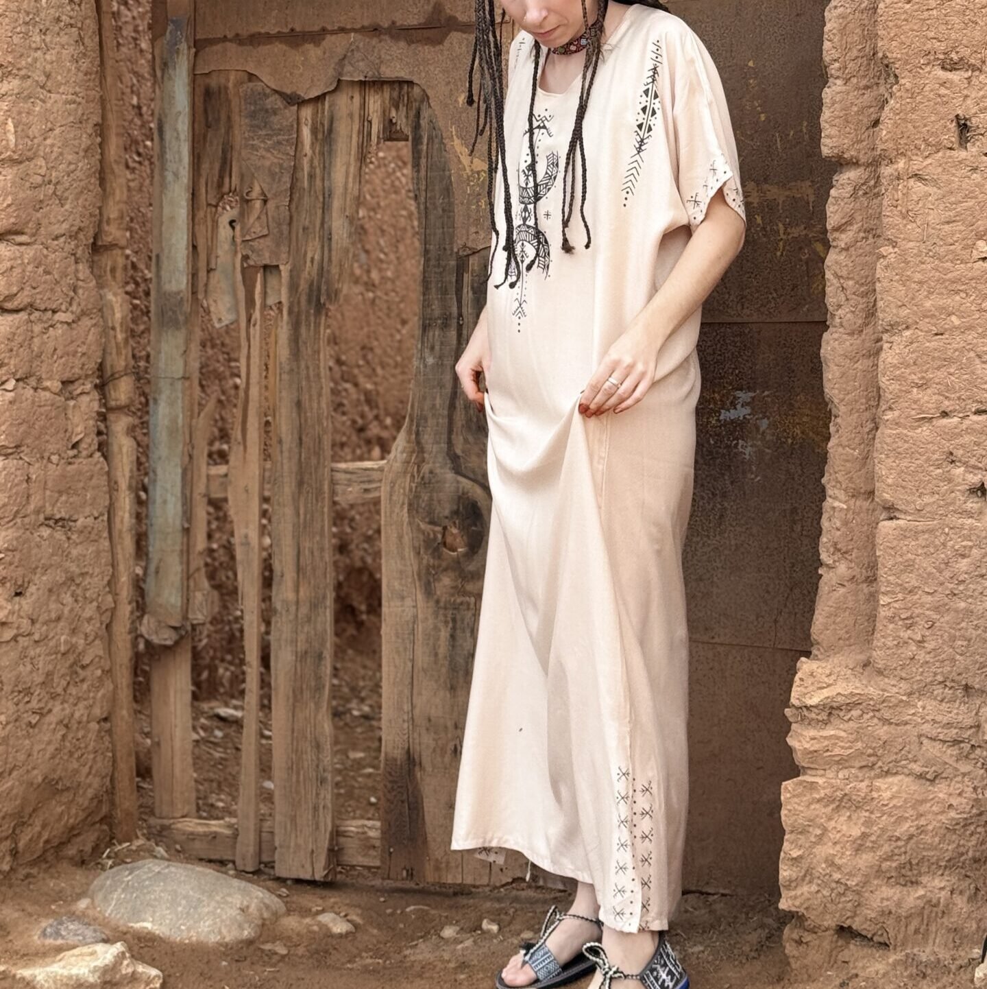 Cream Moroccan Amazigh dress with black geometric embroidery, modeled in a traditional earthen doorway