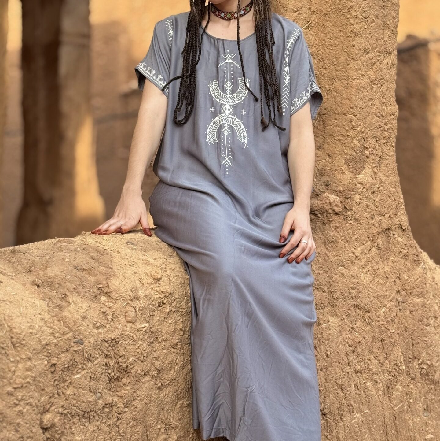 Gray Moroccan Amazigh dress with white geometric embroidery and traditional symbol in an earthen kasbah setting