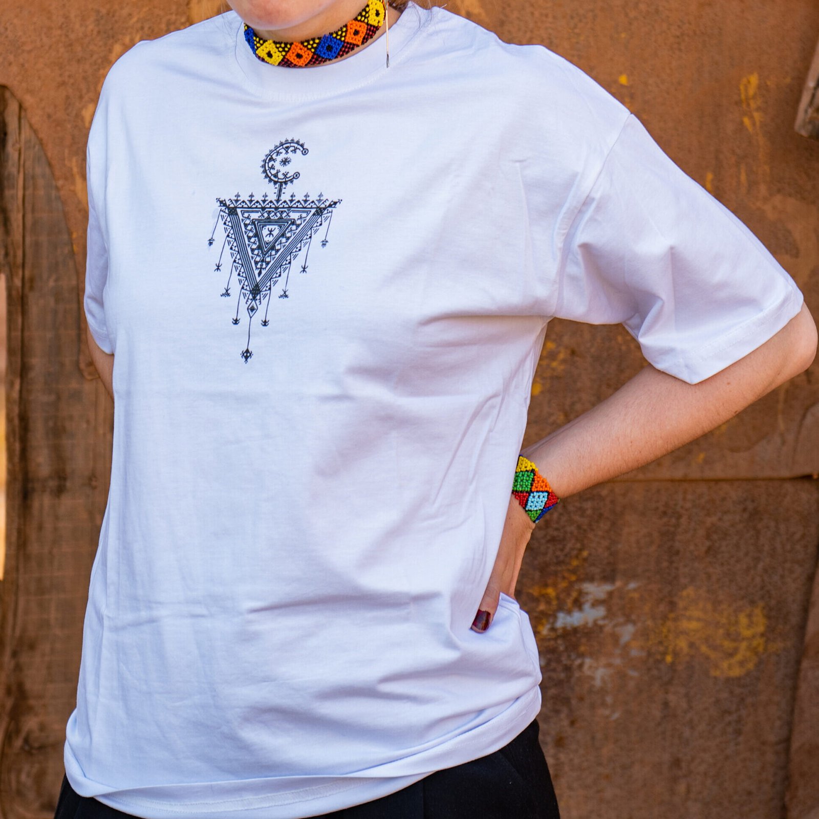 White TASGHNST T-shirt featuring traditional Amazigh symbols and geometric Moroccan artwork