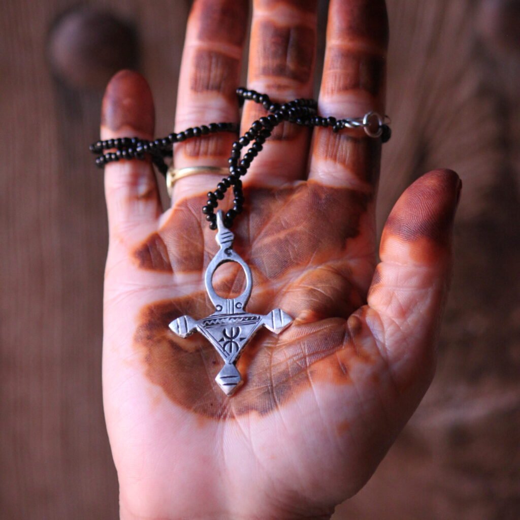 Pendentif amazigh en métal plaqué argent avec motif gravé, monté sur un collier de perles noires.