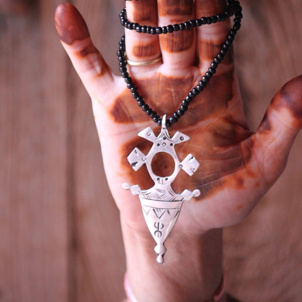 Pendentif amazigh en métal plaqué argent avec motif gravé, monté sur un collier de perles noires.