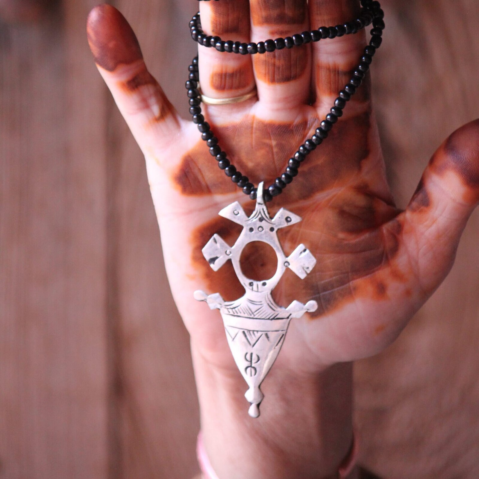Pendentif amazigh en métal plaqué argent avec motif gravé, monté sur un collier de perles noires.