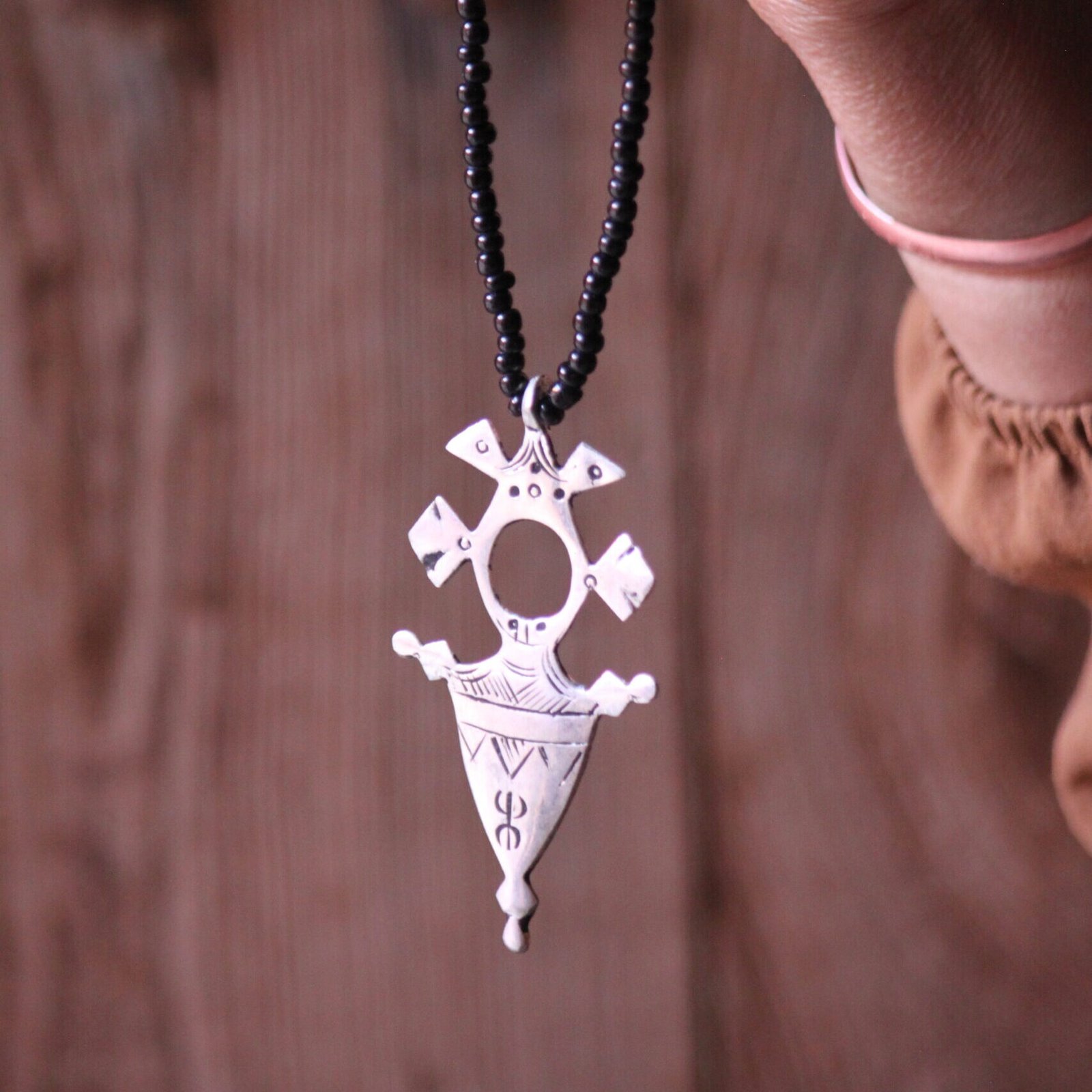 Pendentif amazigh en métal plaqué argent avec motif gravé, monté sur un collier de perles noires.
