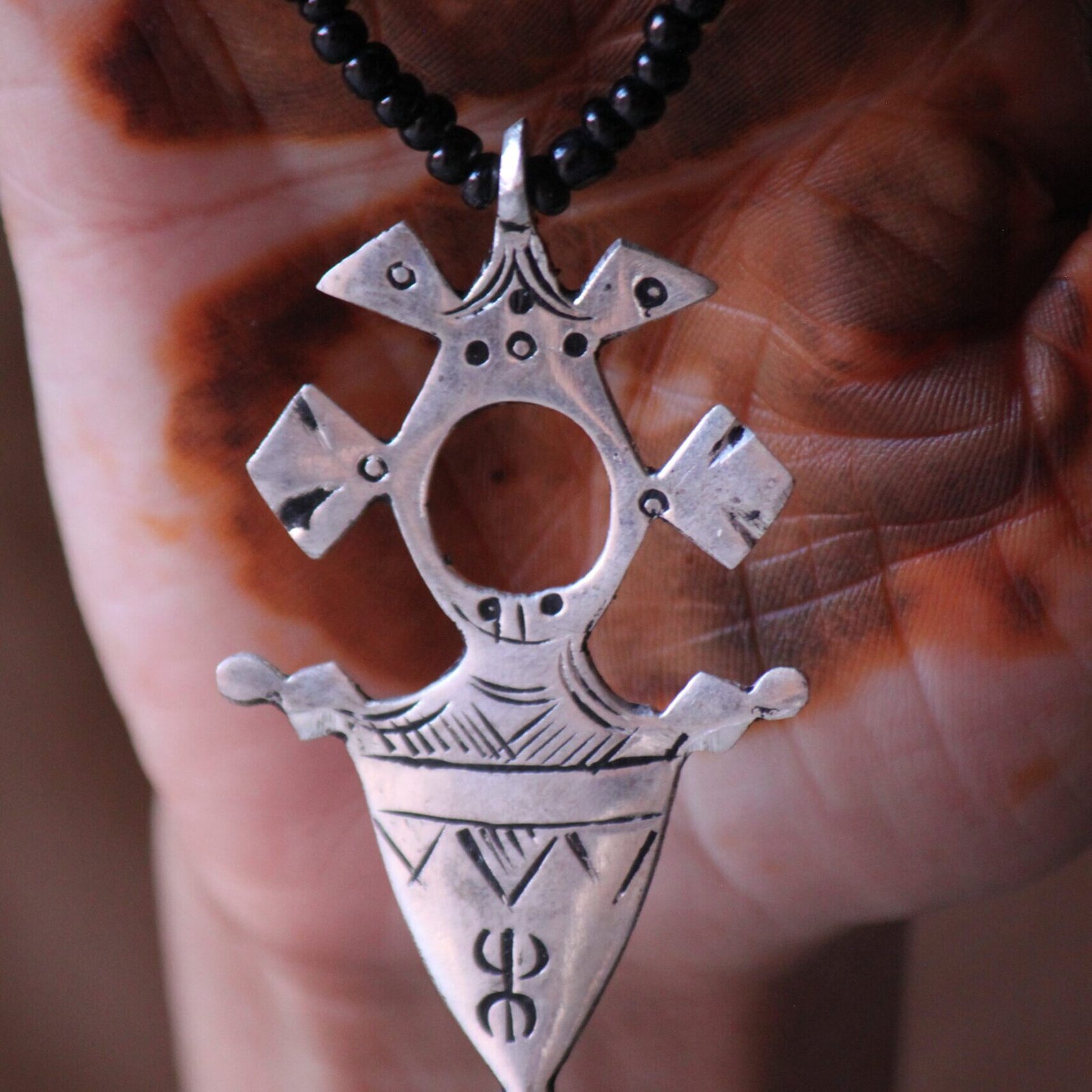 Pendentif amazigh en métal plaqué argent avec motif gravé, monté sur un collier de perles noires.