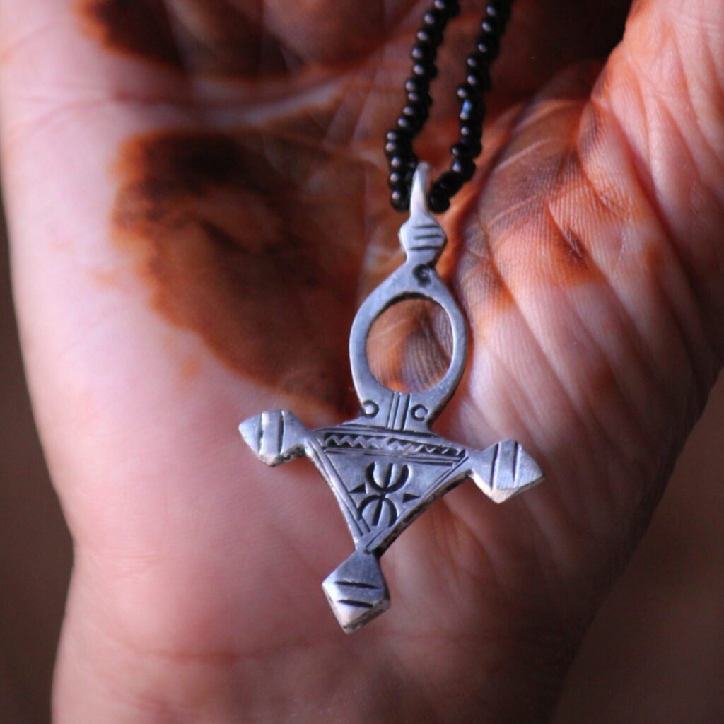 Pendentif amazigh en métal plaqué argent avec motif gravé, monté sur un collier de perles noires.