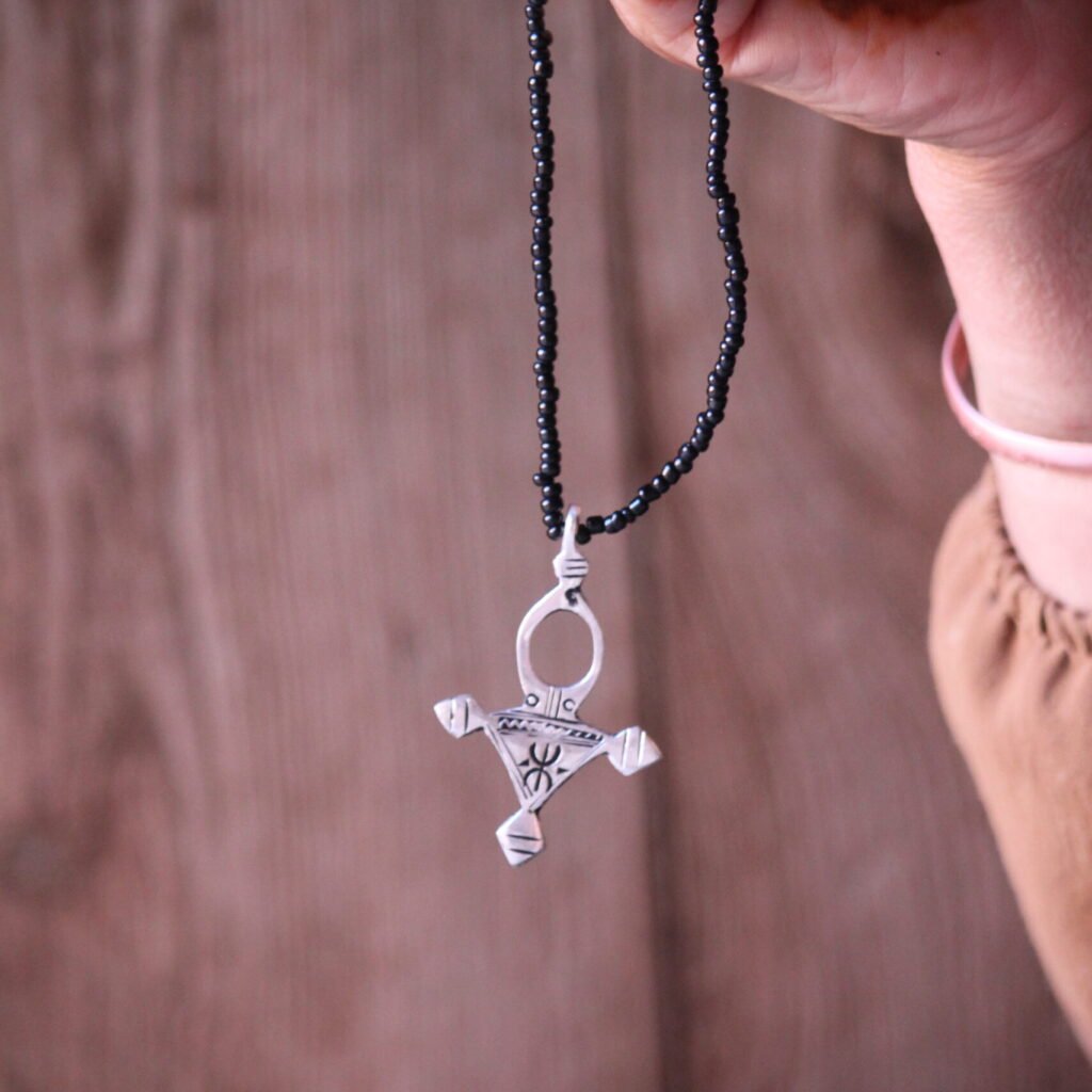 Pendentif amazigh en métal plaqué argent avec motif gravé, monté sur un collier de perles noires.