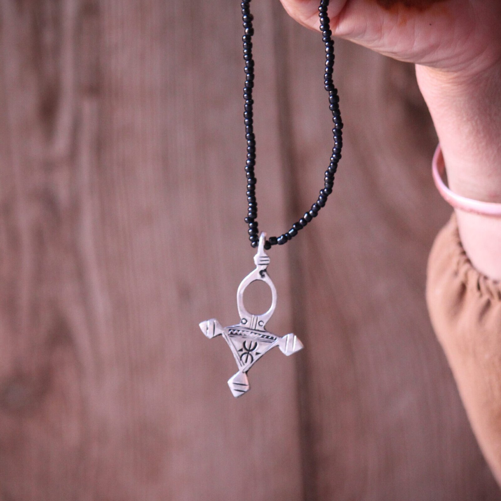 Pendentif amazigh en métal plaqué argent avec motif gravé, monté sur un collier de perles noires.