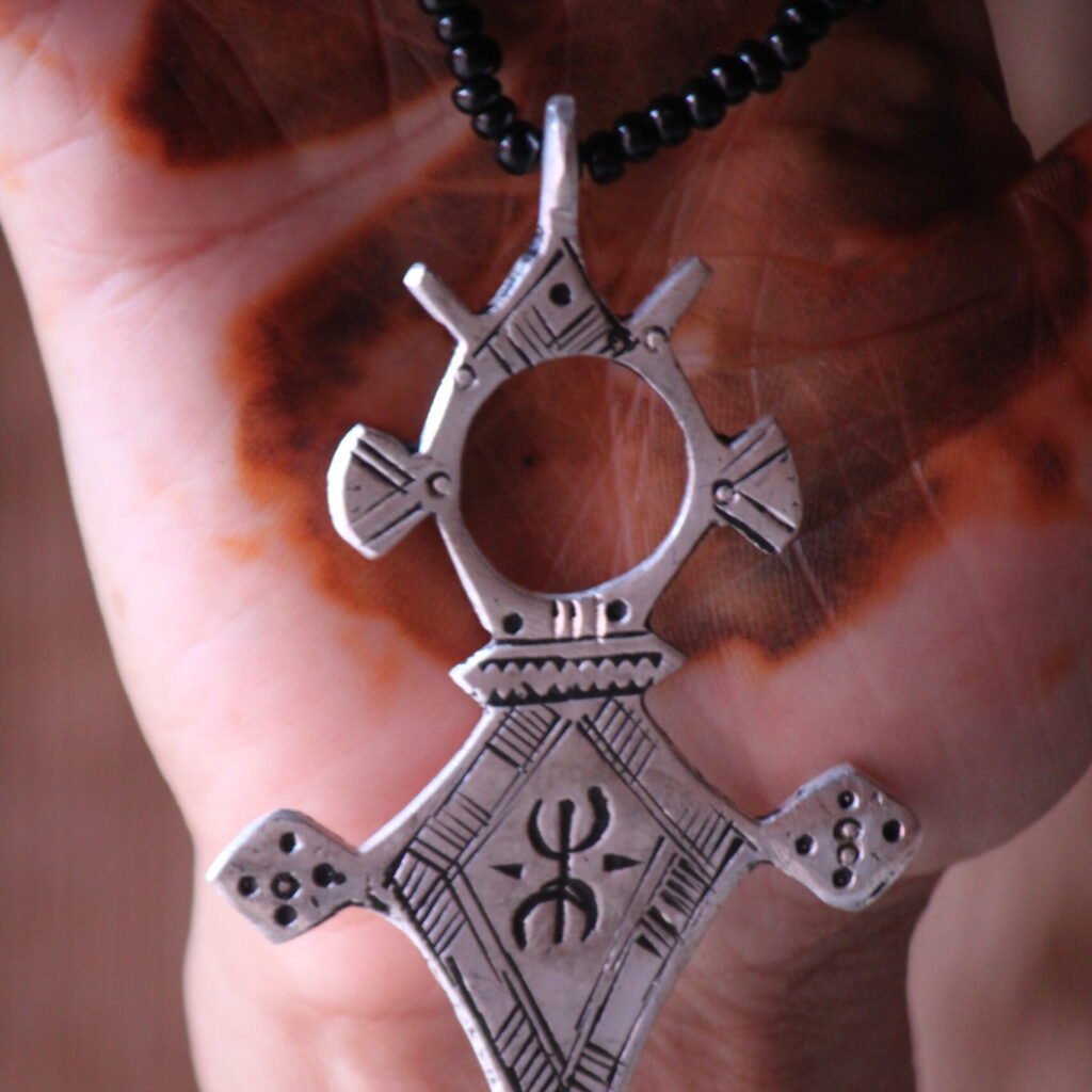 Pendentif amazigh en métal plaqué argent avec motif gravé, monté sur un collier de perles noires.