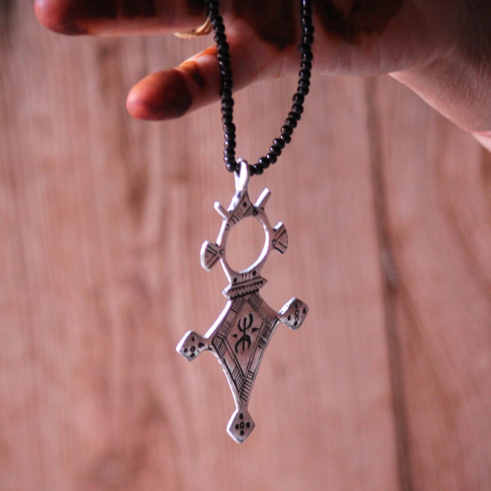 Pendentif amazigh en métal plaqué argent avec motif gravé, monté sur un collier de perles noires.