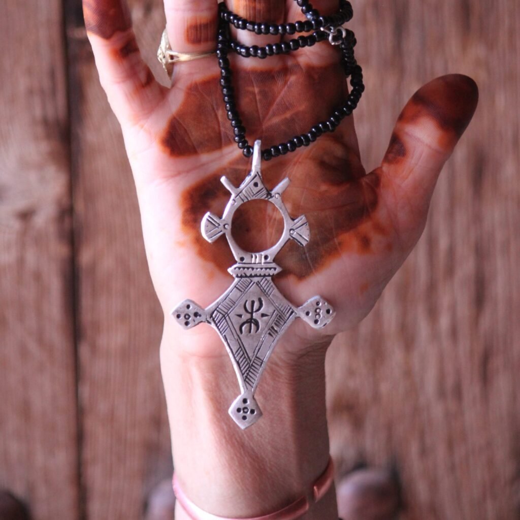 Pendentif amazigh en métal plaqué argent avec motif gravé, monté sur un collier de perles noires.