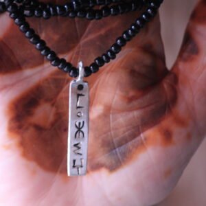 Pendentif amazigh en métal plaqué argent avec motif gravé, monté sur un collier de perles noires.