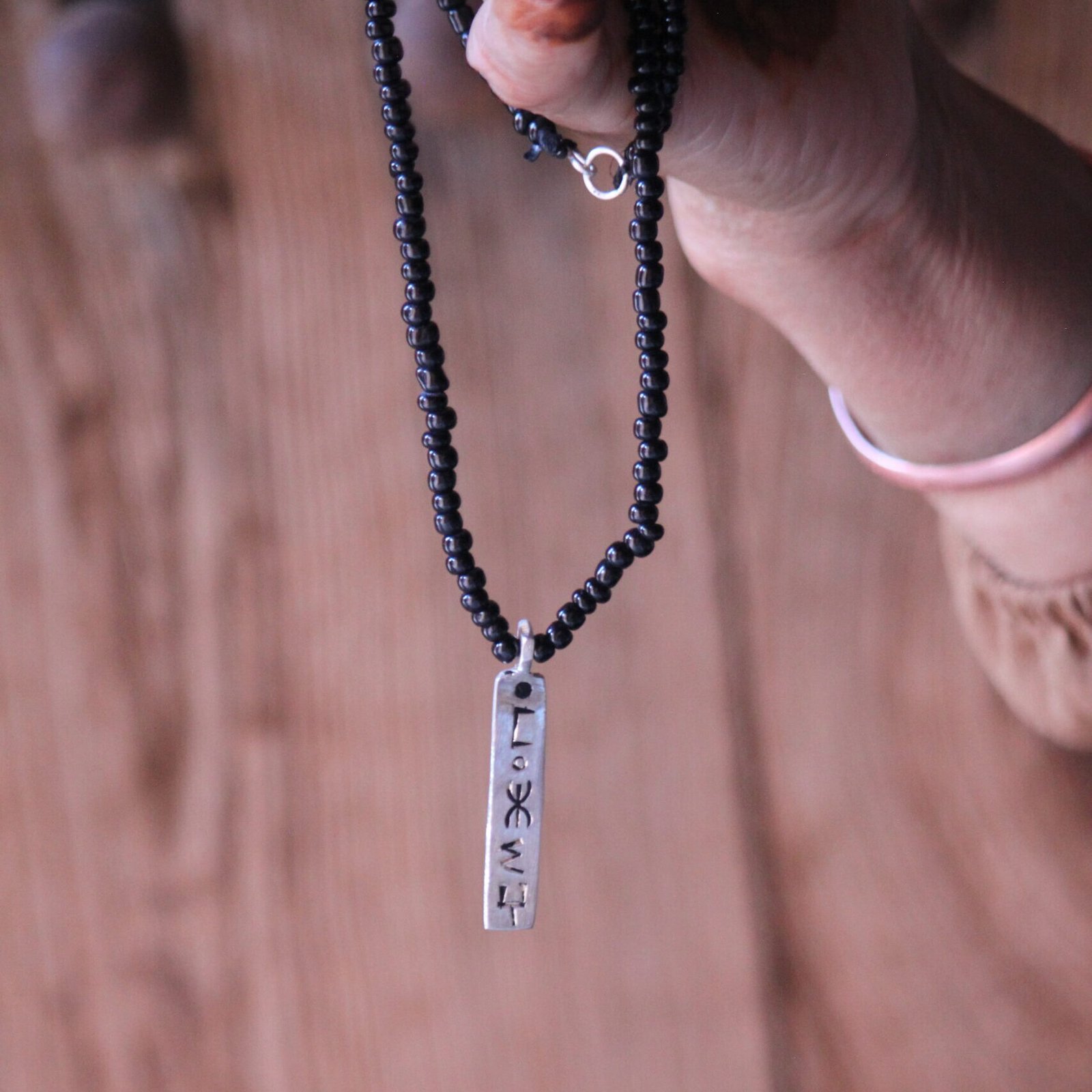 Pendentif amazigh en métal plaqué argent avec motif gravé, monté sur un collier de perles noires.