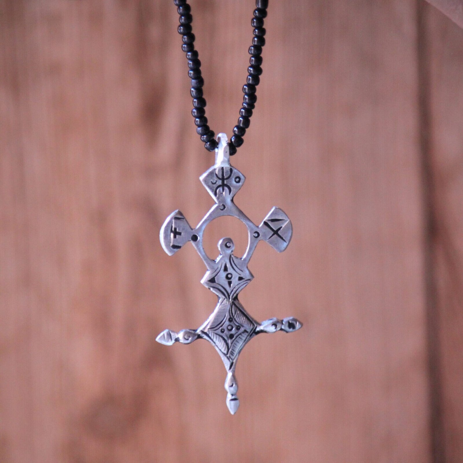 Pendentif amazigh en métal plaqué argent avec motif gravé, monté sur un collier de perles noires.