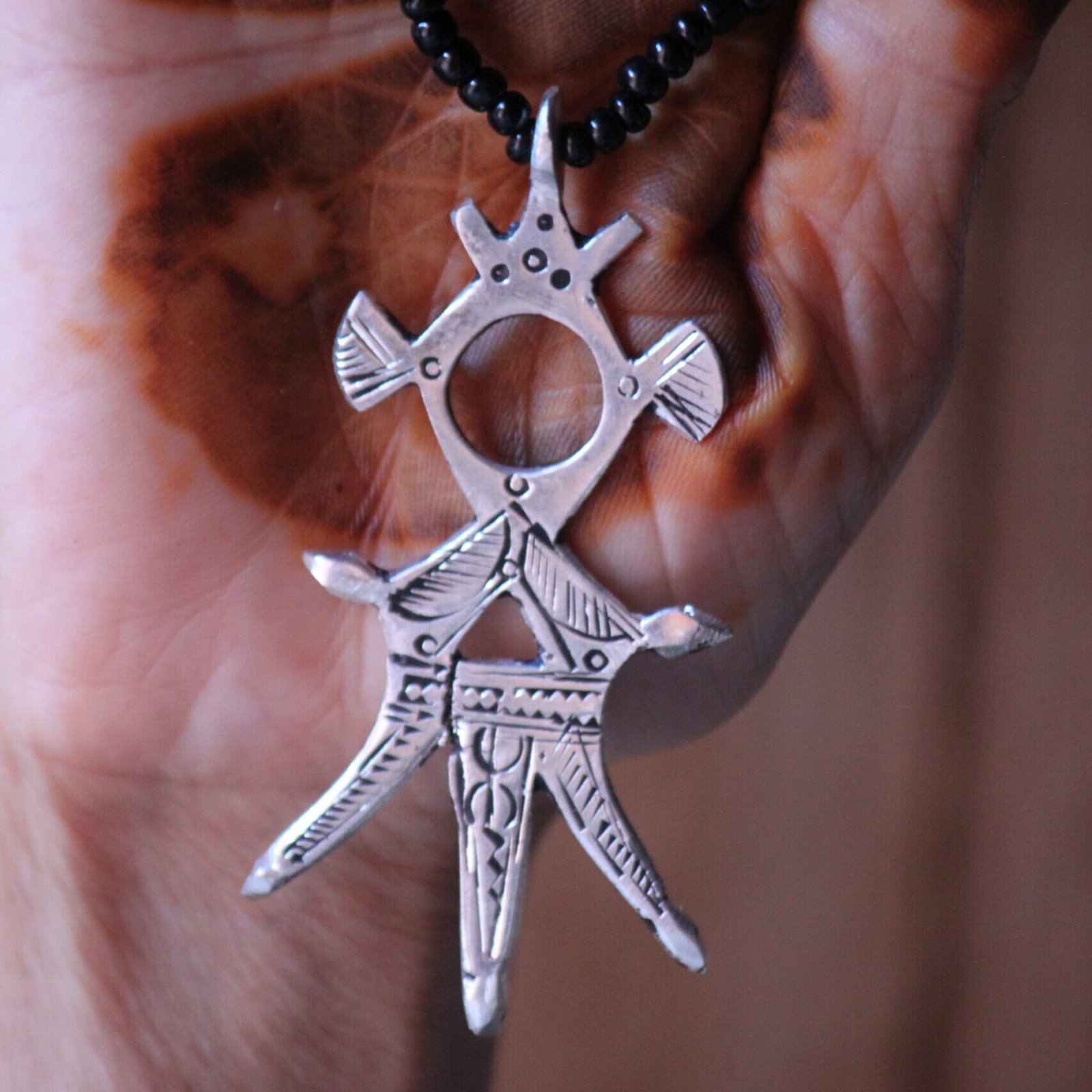Pendentif amazigh en métal plaqué argent avec motif gravé, monté sur un collier de perles noires.