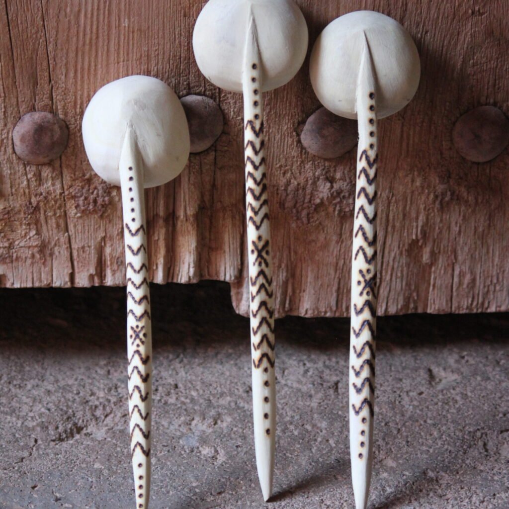 Trois cuillères artisanales en bois, sculptées et décorées de motifs amazighs, devant une porte traditionnelle.