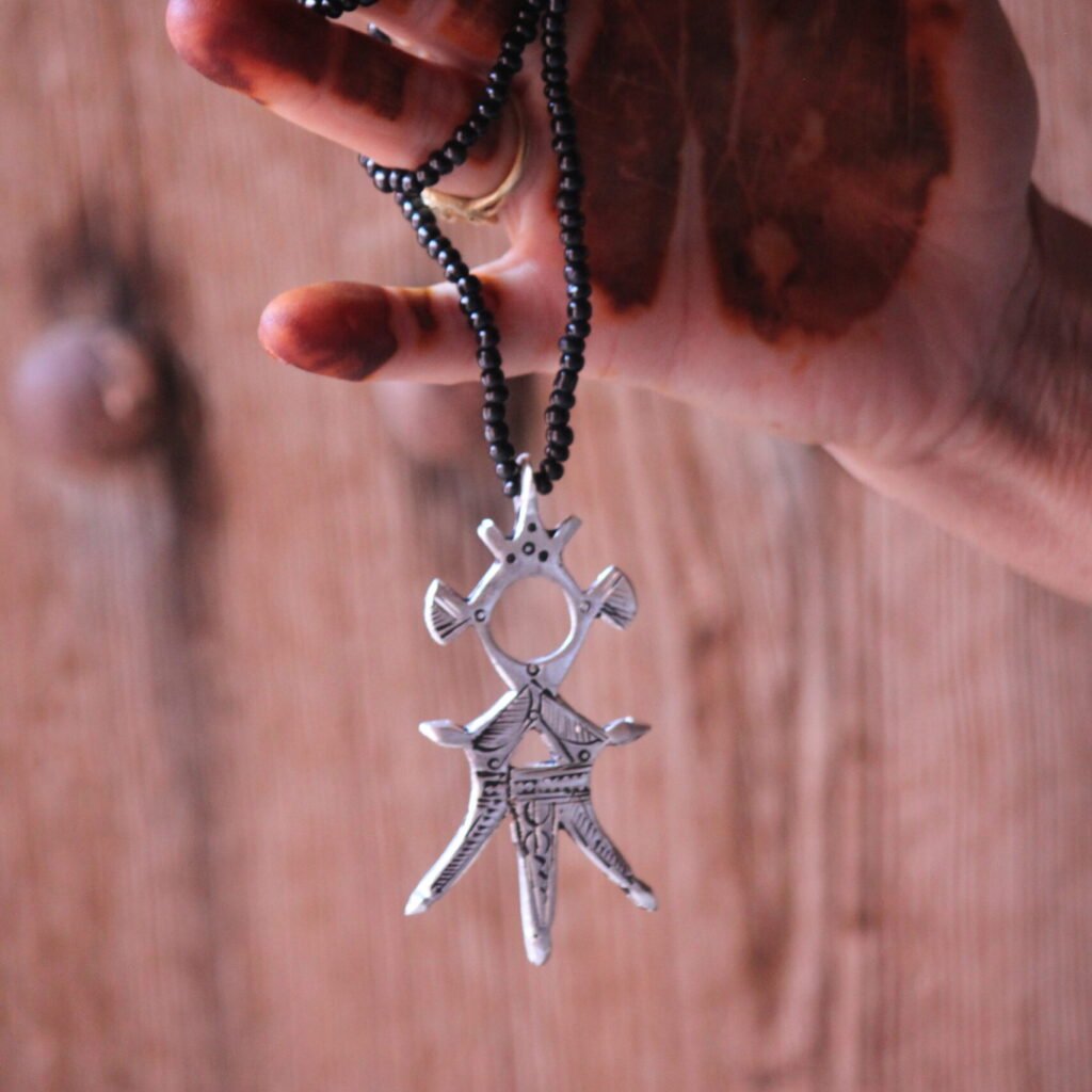 Pendentif amazigh en métal plaqué argent avec motif gravé, monté sur un collier de perles noires.