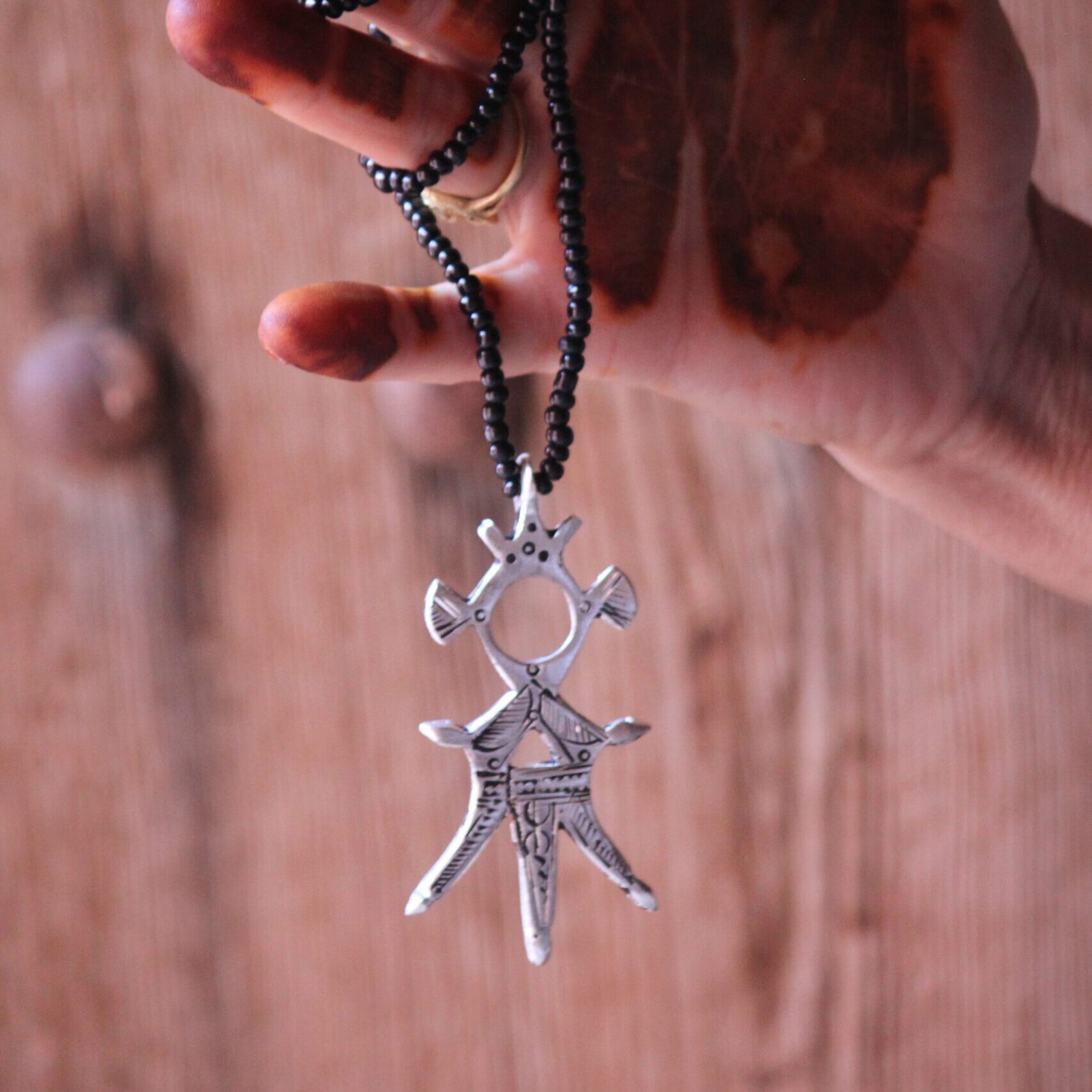 Pendentif amazigh en métal plaqué argent avec motif gravé, monté sur un collier de perles noires.