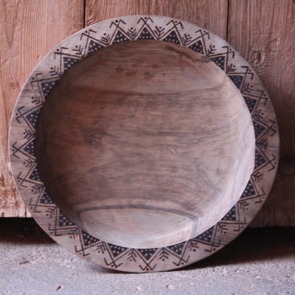 Grande assiette artisanale en bois, décorée de motifs géométriques amazighs sur le pourtour.
