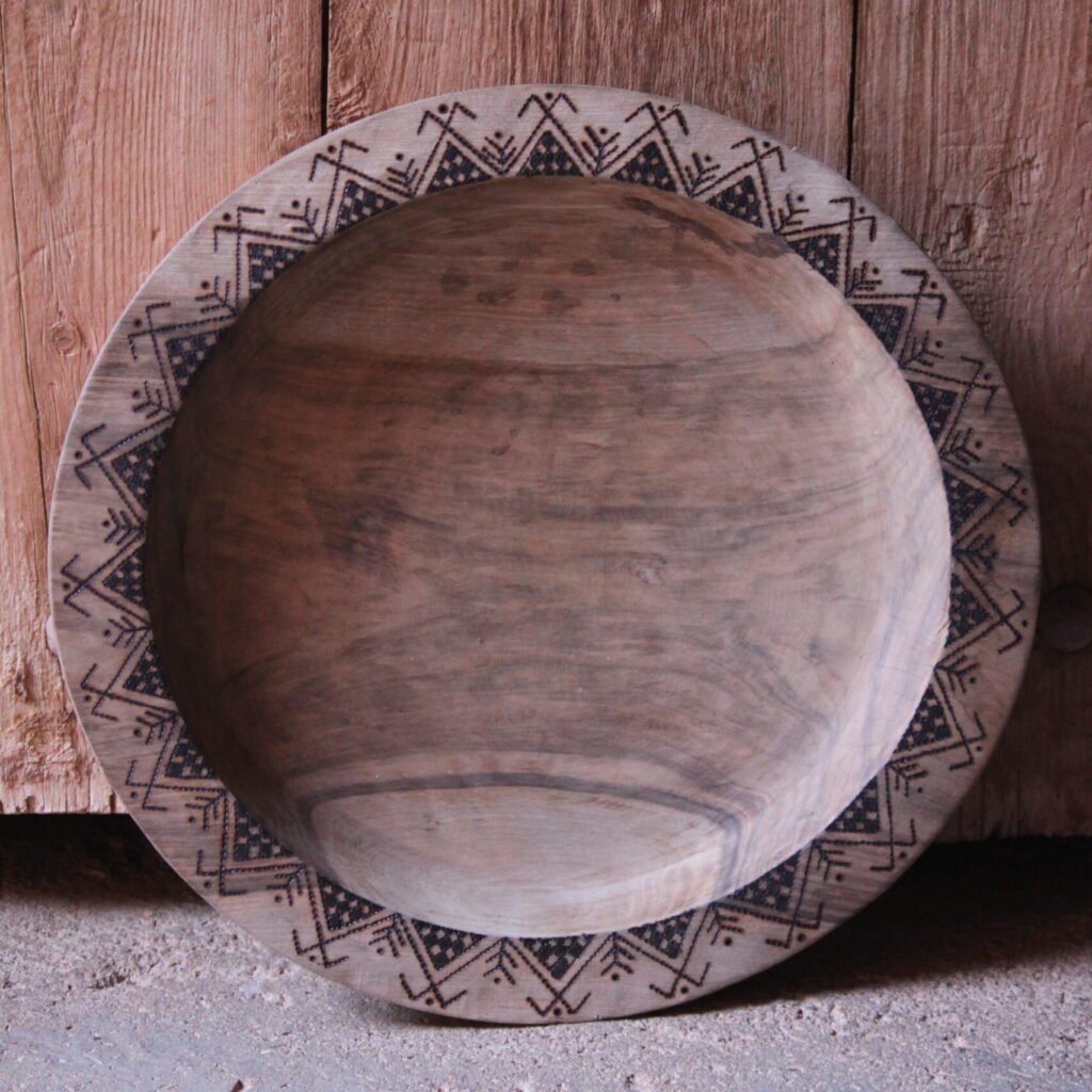 Grande assiette artisanale en bois de noyer, décorée de motifs géométriques amazighs sur le pourtour.
