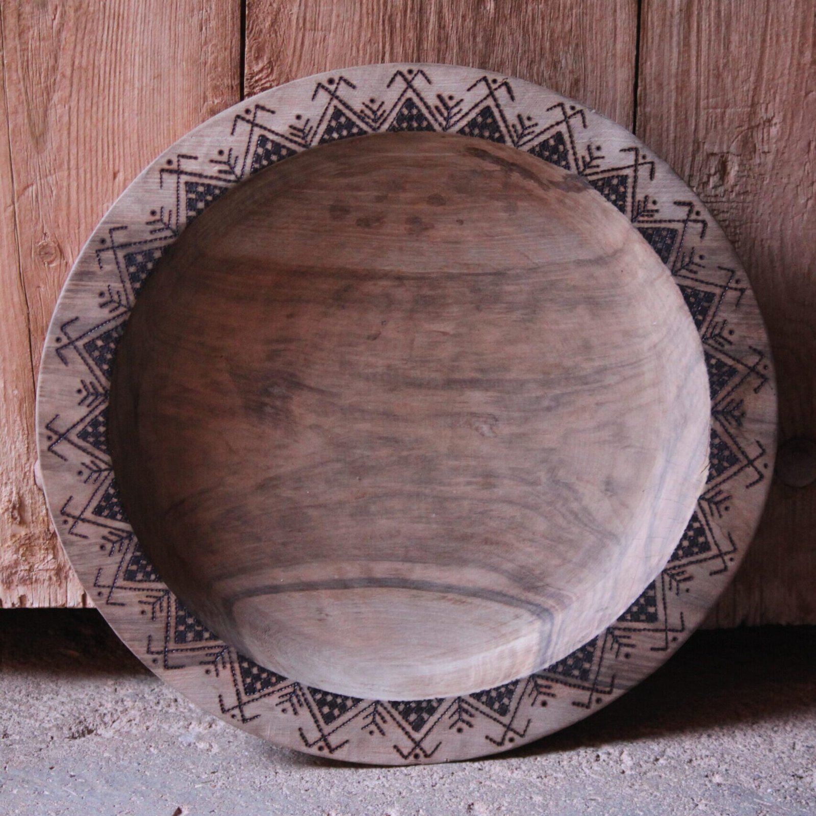 Grande assiette artisanale en bois de noyer, décorée de motifs géométriques amazighs sur le pourtour.