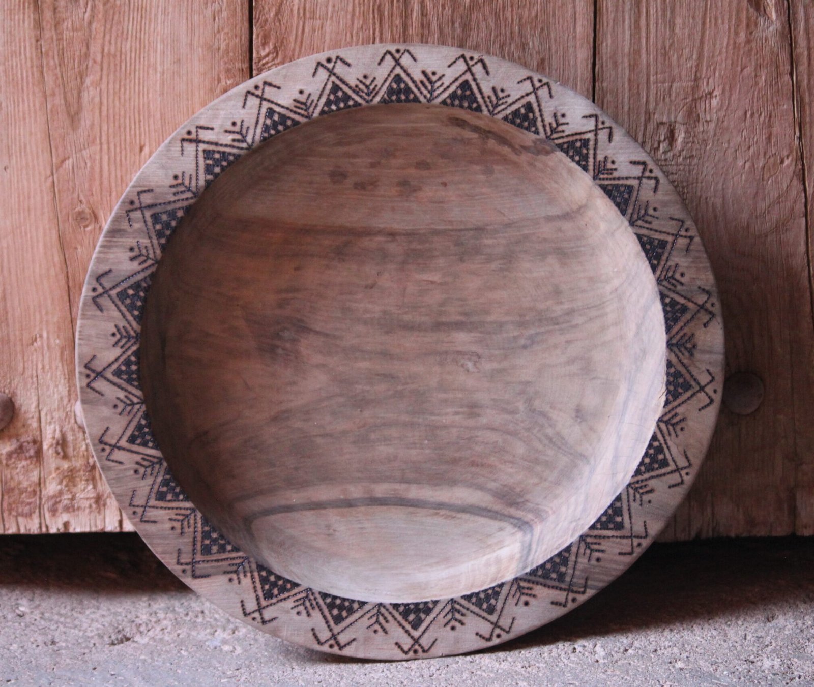 Grande assiette artisanale en bois de noyer, décorée de motifs géométriques amazighs sur le pourtour.