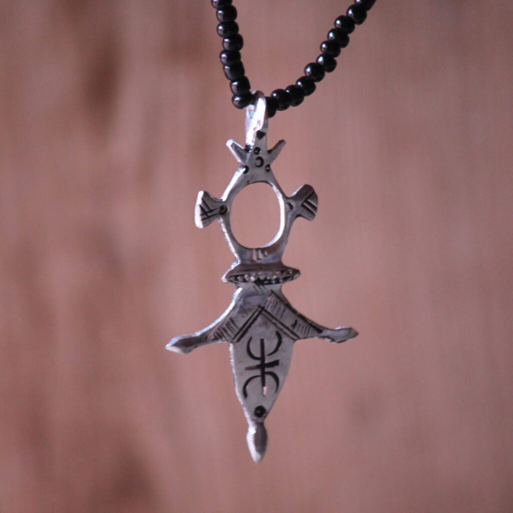 Pendentif amazigh en métal plaqué argent avec motif gravé, monté sur un collier de perles noires.