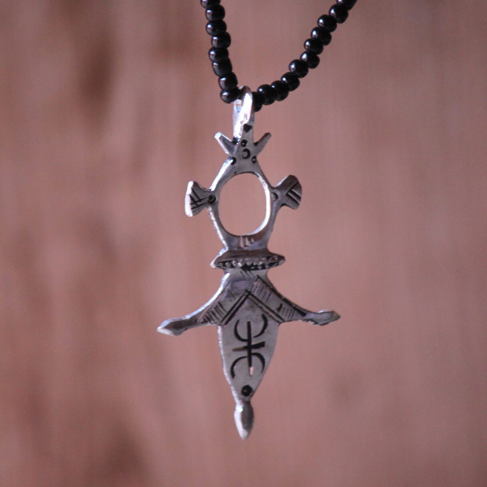 Pendentif amazigh en métal plaqué argent avec motif gravé, monté sur un collier de perles noires.