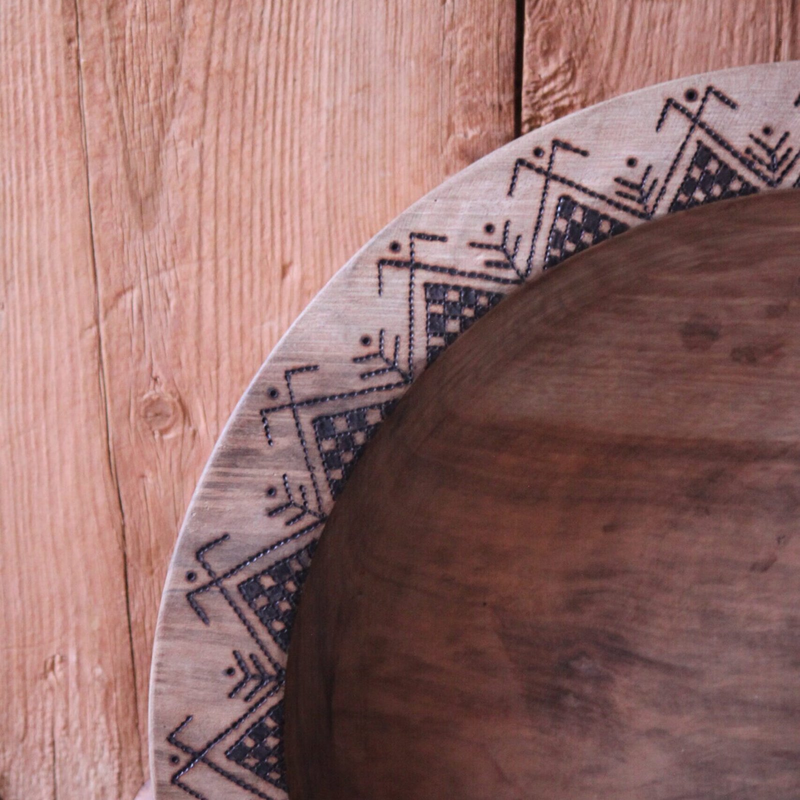 Grande assiette artisanale en bois de noyer, décorée de motifs géométriques amazighs sur le pourtour.