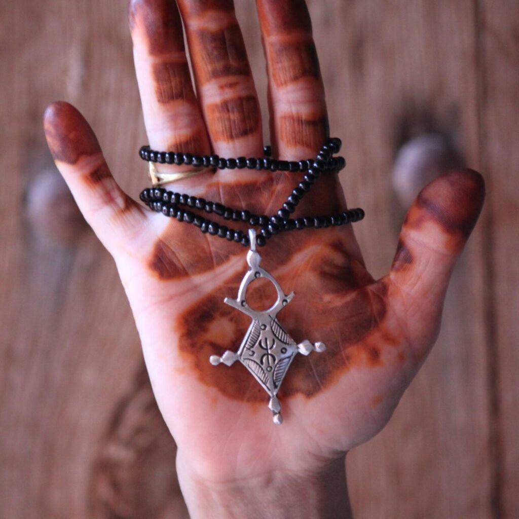 Pendentif amazigh en métal plaqué argent avec motif gravé, monté sur un collier de perles noires.