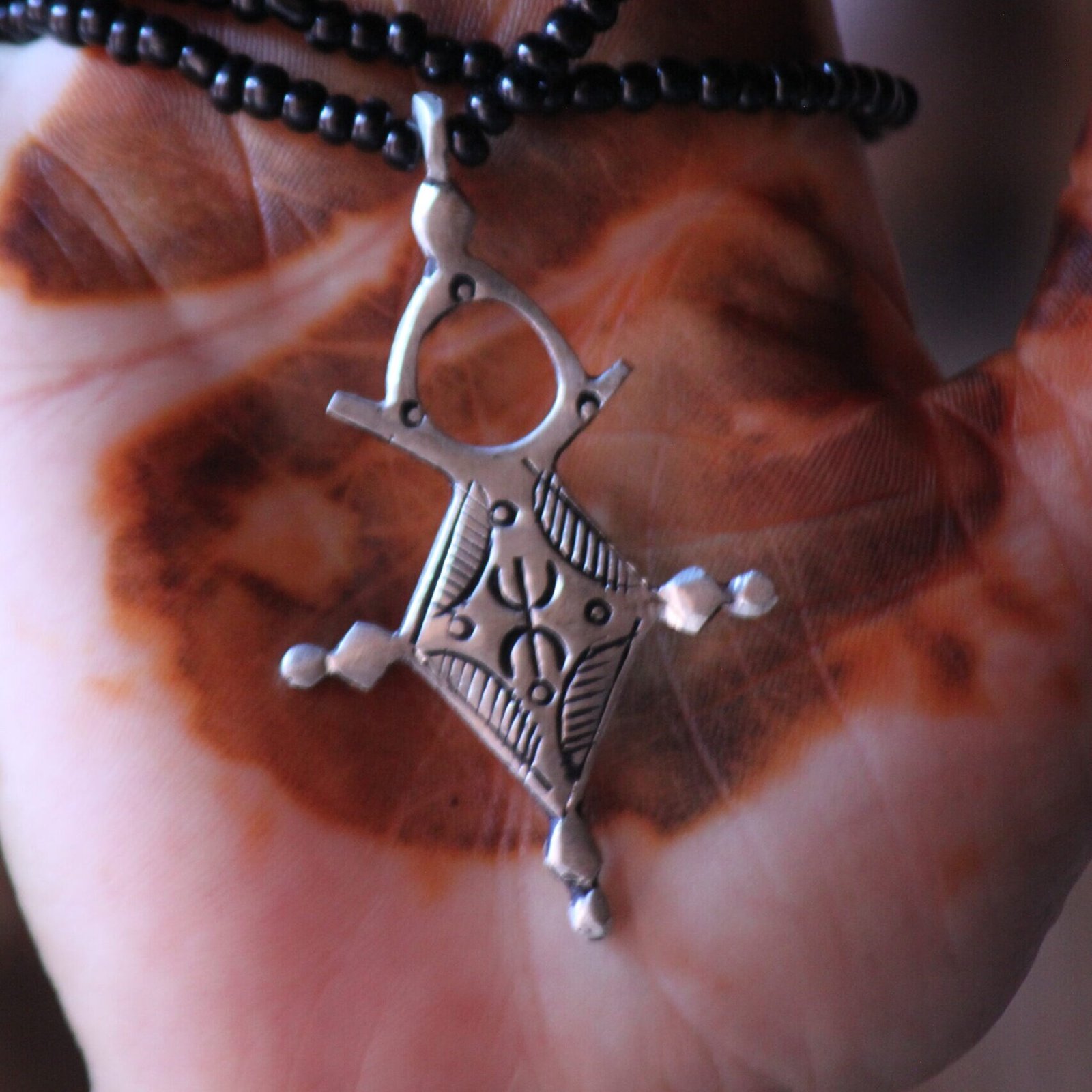 Pendentif amazigh en métal plaqué argent avec motif gravé, monté sur un collier de perles noires.