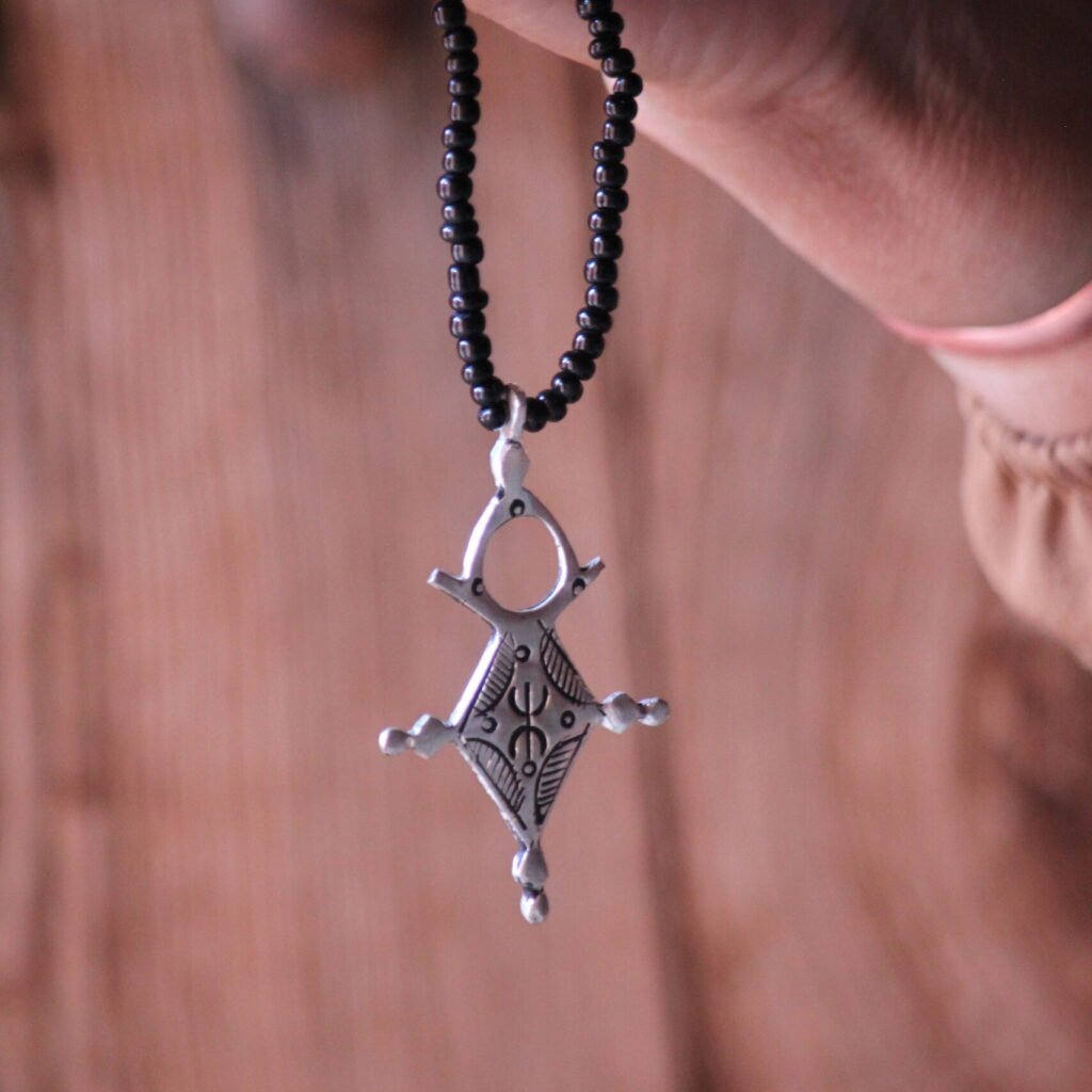 Pendentif amazigh en métal plaqué argent avec motif gravé, monté sur un collier de perles noires.