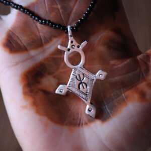 Pendentif amazigh en métal plaqué argent avec motif gravé, monté sur un collier de perles noires.