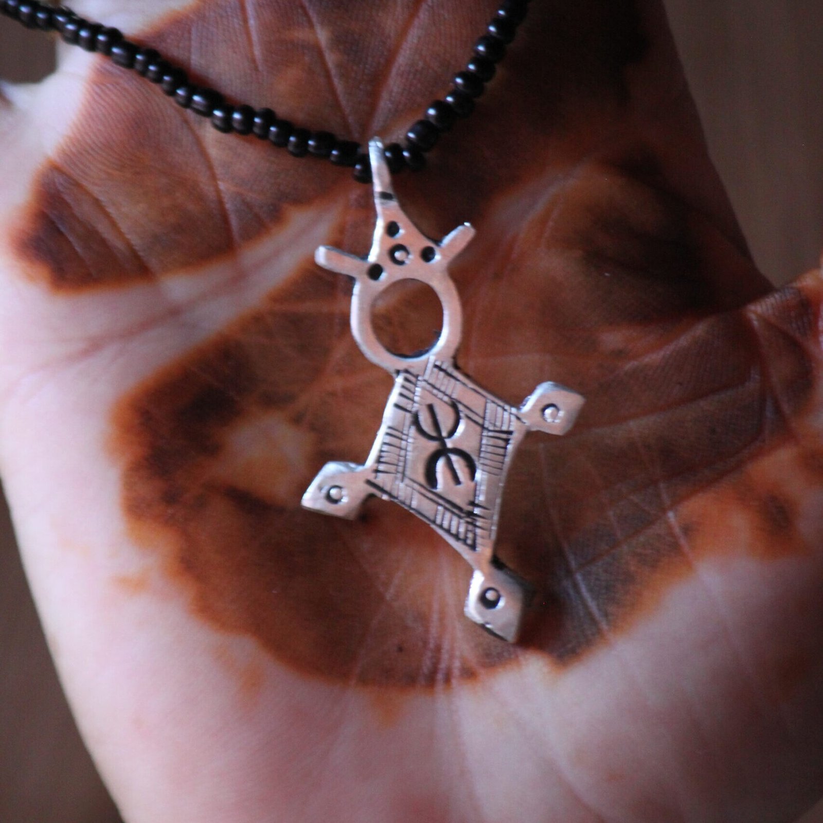 Pendentif amazigh en métal plaqué argent avec motif gravé, monté sur un collier de perles noires.