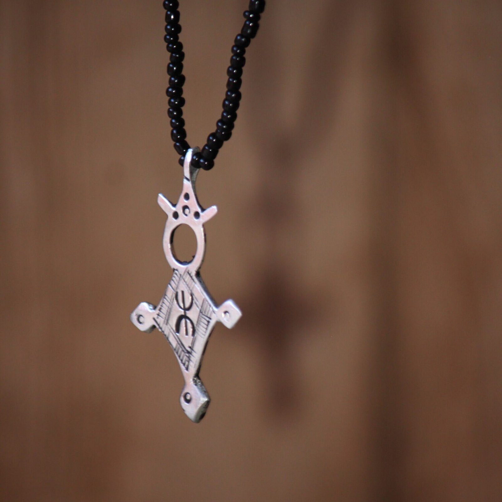 Pendentif amazigh en métal plaqué argent avec motif gravé, monté sur un collier de perles noires.
