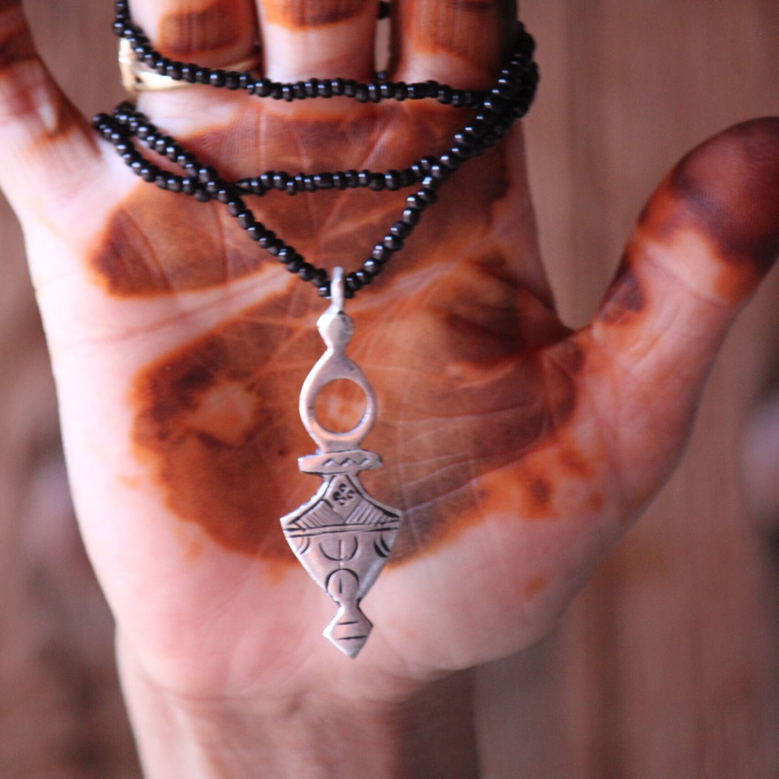 Pendentif amazigh en métal plaqué argent avec motif gravé, monté sur un collier de perles noires.