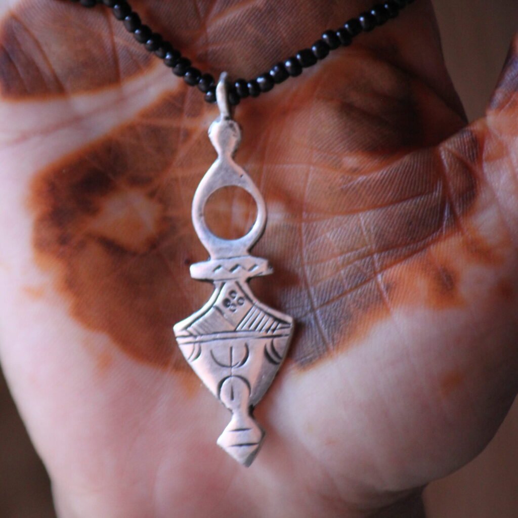 Pendentif amazigh en métal plaqué argent avec motif gravé, monté sur un collier de perles noires.
