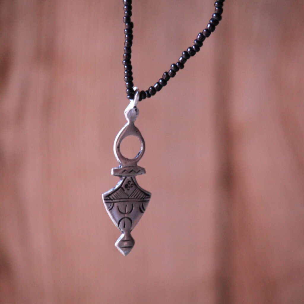 Pendentif amazigh en métal plaqué argent avec motif gravé, monté sur un collier de perles noires.