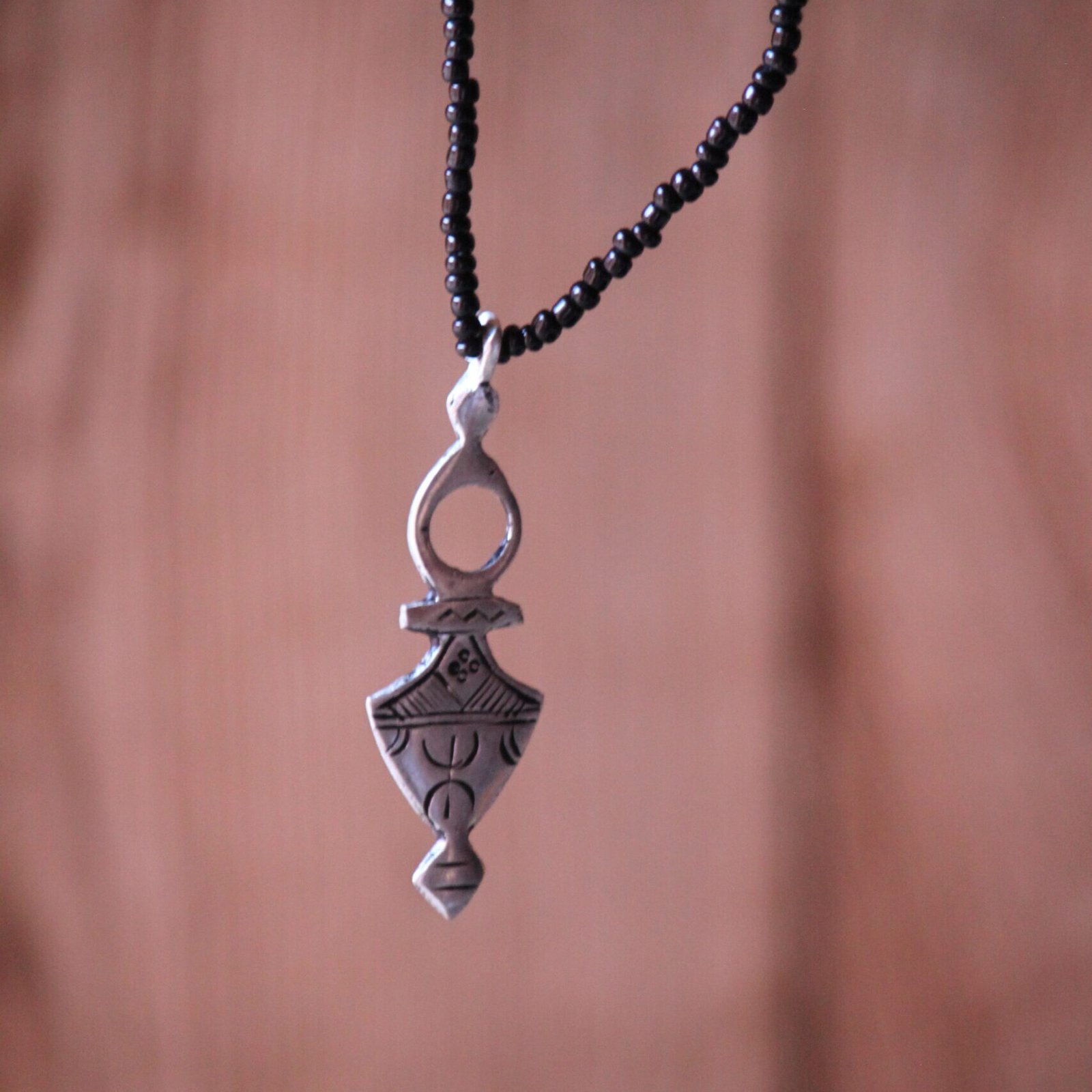 Pendentif amazigh en métal plaqué argent avec motif gravé, monté sur un collier de perles noires.