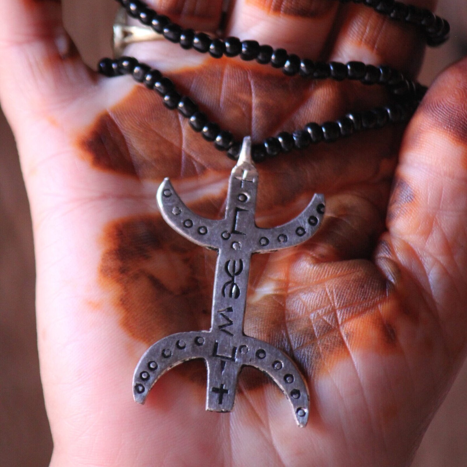 Pendentif amazigh en métal plaqué argent avec motif gravé, monté sur un collier de perles noires.