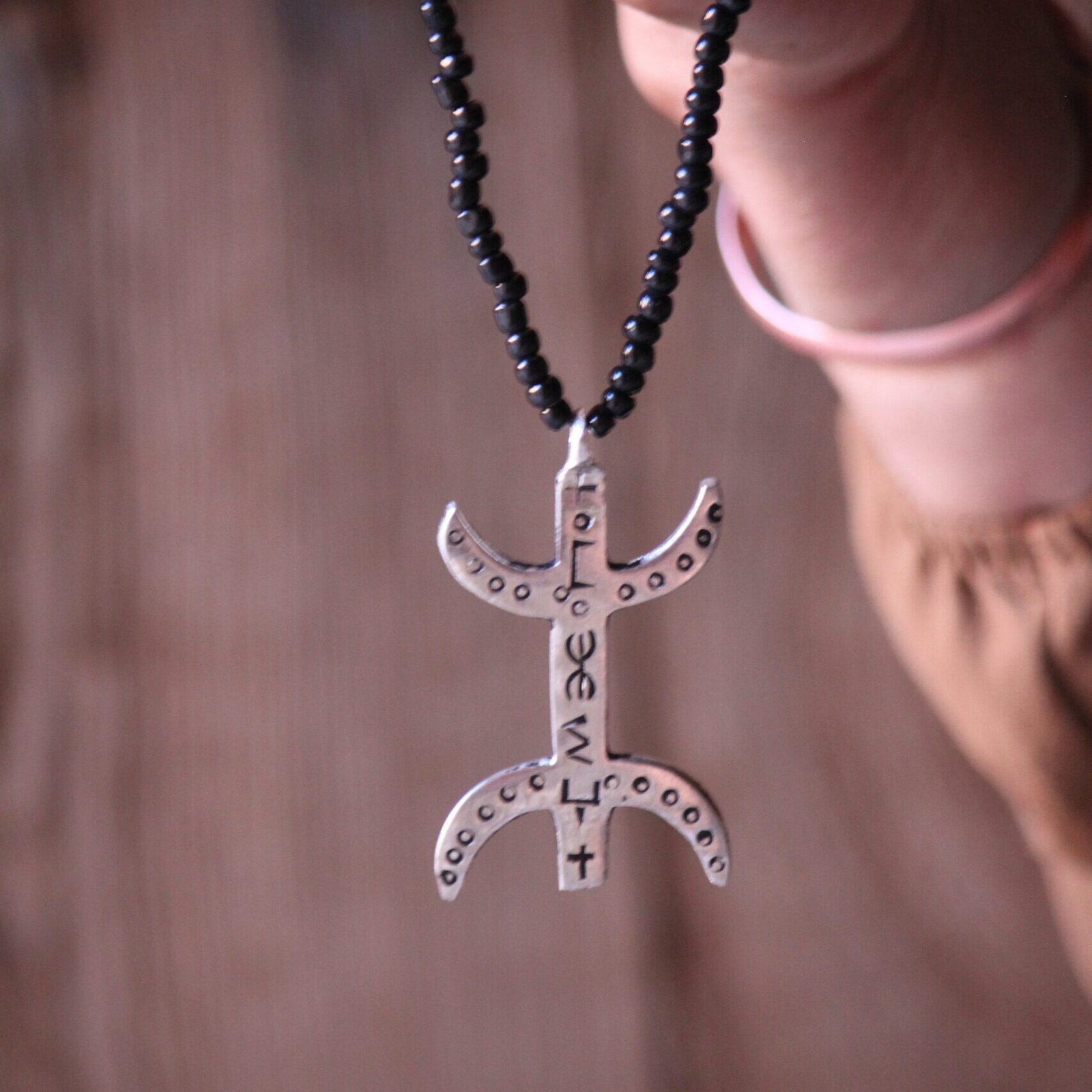 Pendentif amazigh en métal plaqué argent avec motif gravé, monté sur un collier de perles noires.