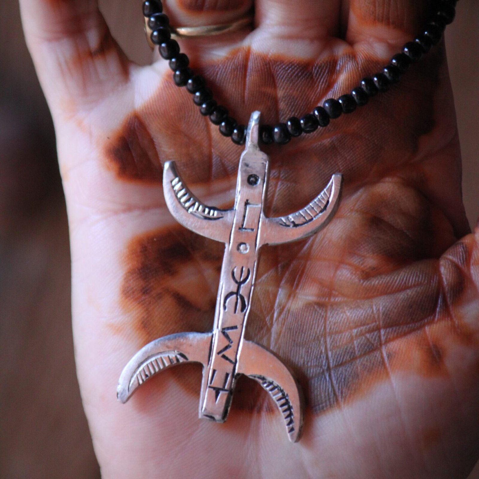Pendentif amazigh en métal plaqué argent avec motif gravé, monté sur un collier de perles noires.