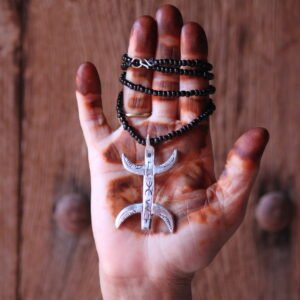 Pendentif amazigh en métal plaqué argent avec motif gravé, monté sur un collier de perles noires.
