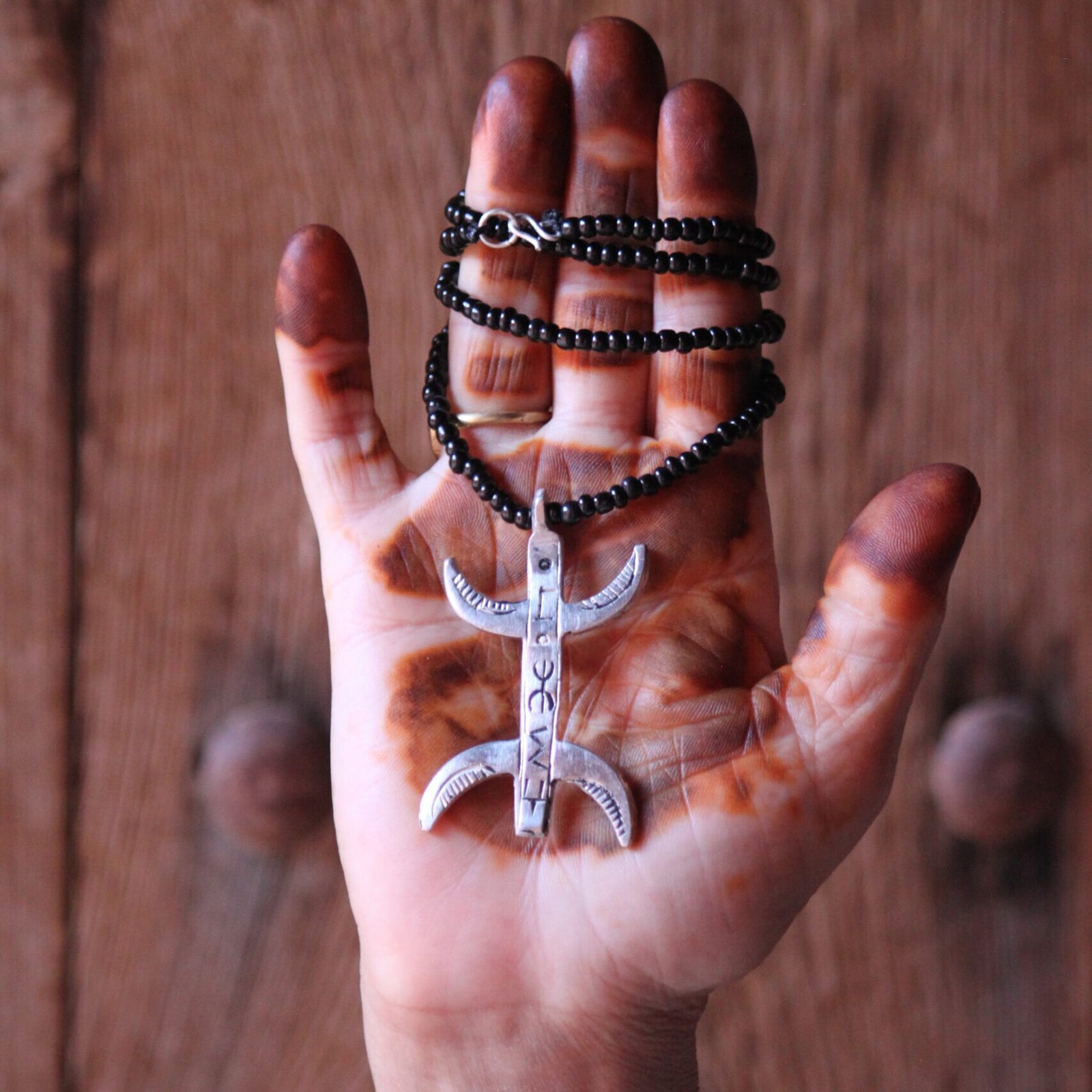 Pendentif amazigh en métal plaqué argent avec motif gravé, monté sur un collier de perles noires.