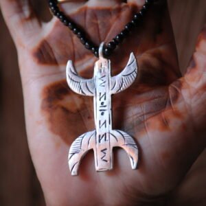 Pendentif amazigh en métal plaqué argent avec motif gravé, monté sur un collier de perles noires.