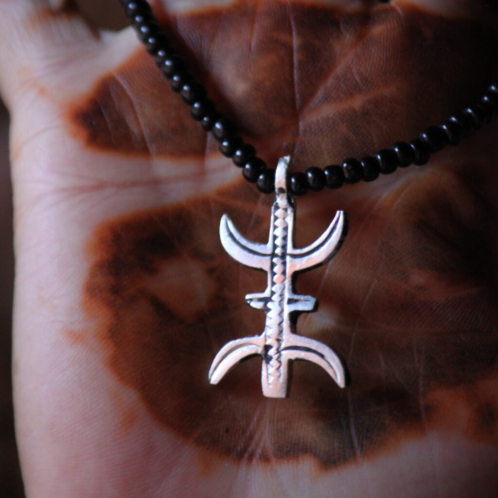 Pendentif amazigh en métal plaqué argent avec motif gravé, monté sur un collier de perles noires.