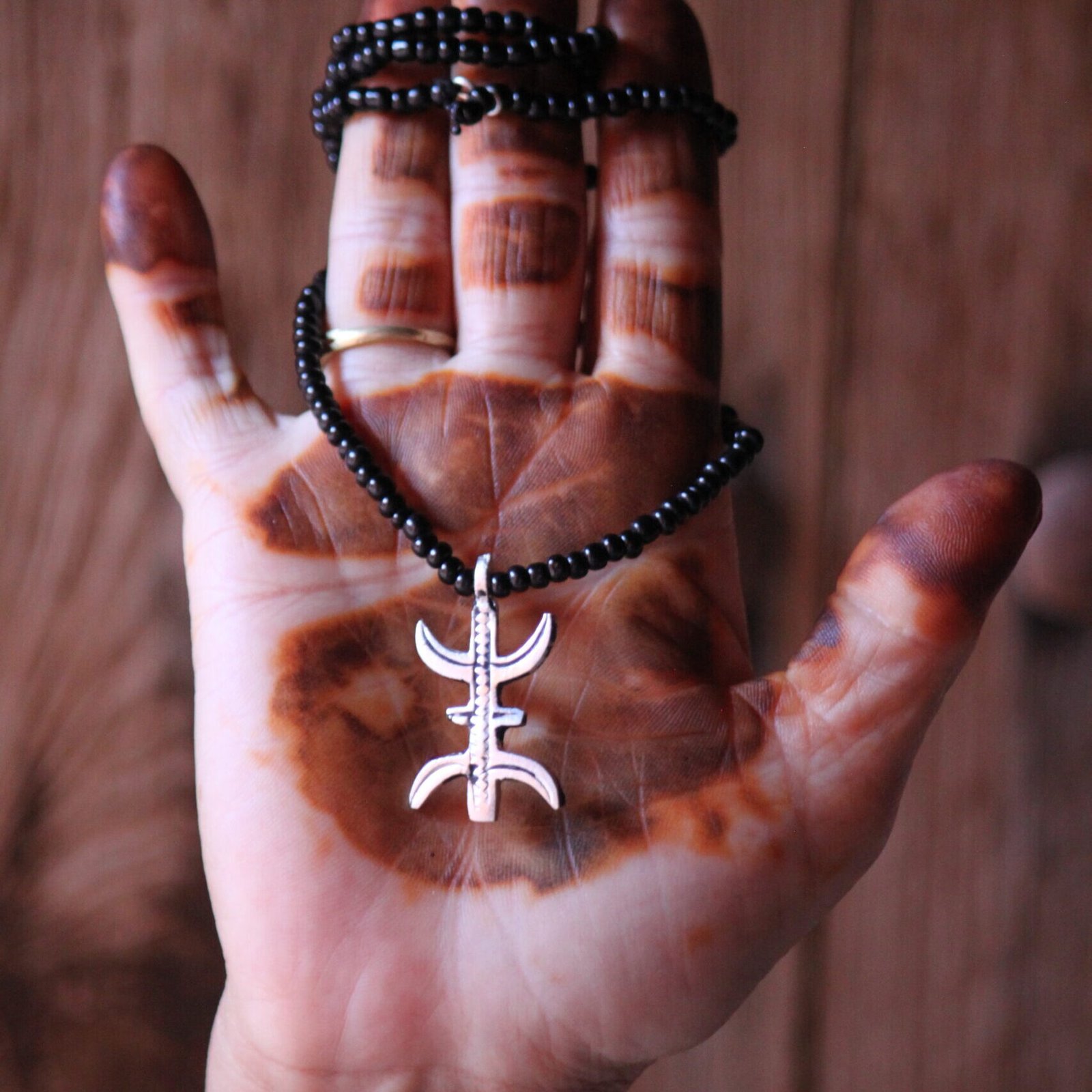 Pendentif amazigh en métal plaqué argent avec motif gravé, monté sur un collier de perles noires.