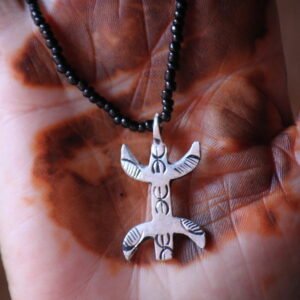 Pendentif amazigh en métal plaqué argent avec motif gravé, monté sur un collier de perles noires.