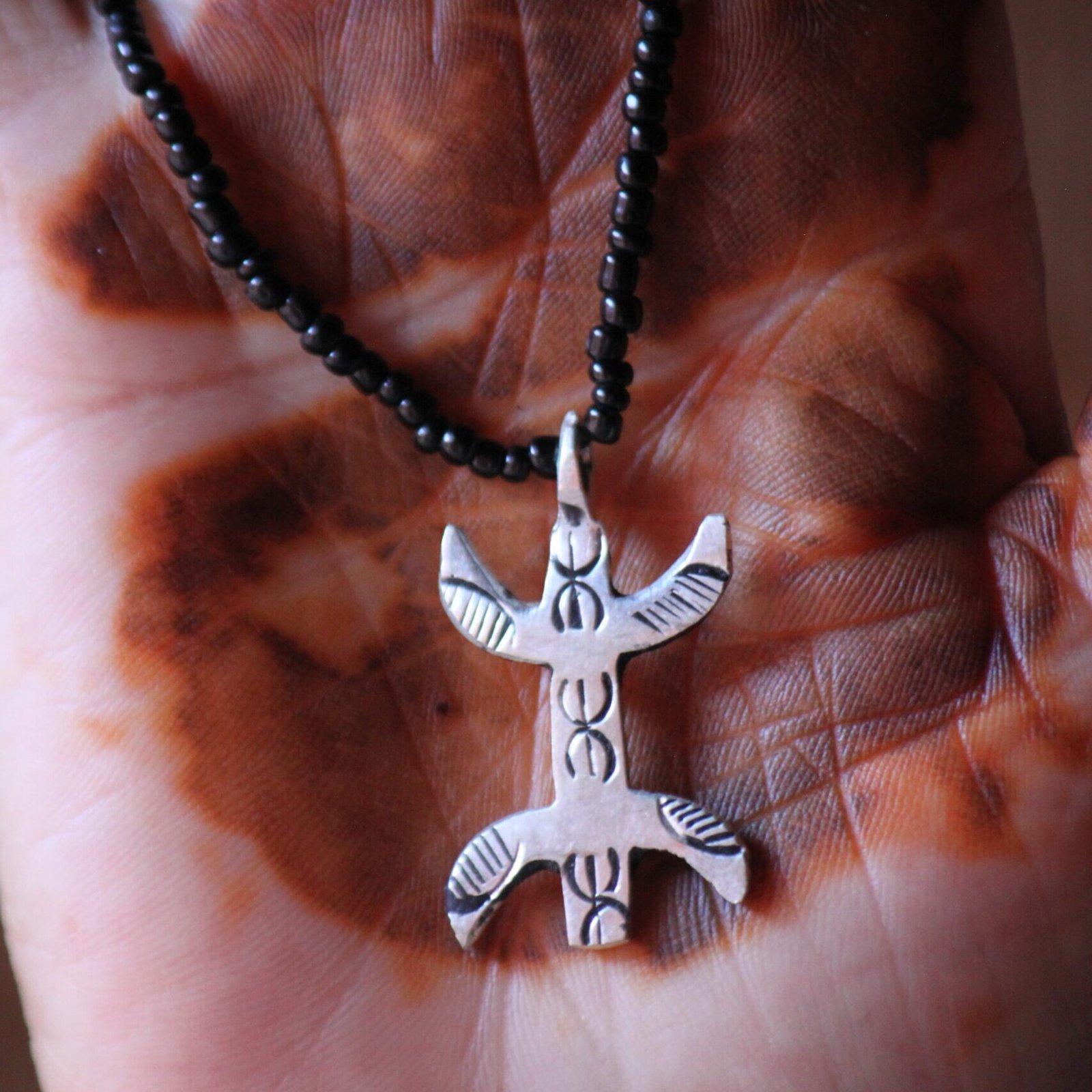 Pendentif amazigh en métal plaqué argent avec motif gravé, monté sur un collier de perles noires.